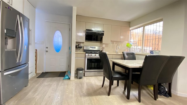 kitchen with light wood-style flooring, a sink, appliances with stainless steel finishes, exhaust hood, and light countertops