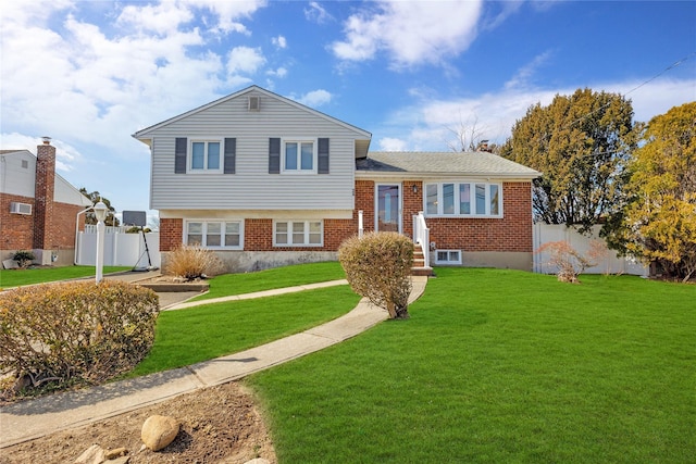 tri-level home featuring brick siding, a front lawn, and fence