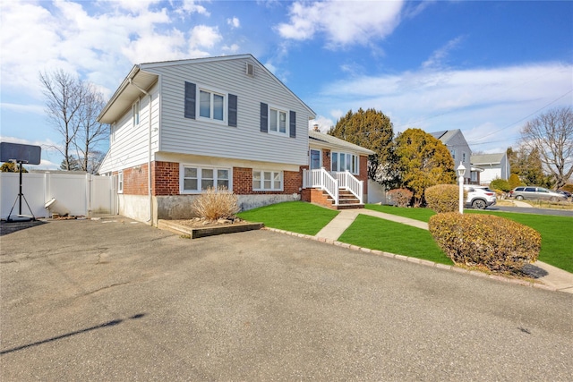 tri-level home featuring a front lawn, a gate, fence, and brick siding