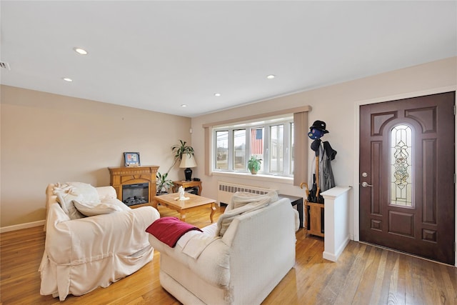 living area with radiator, baseboards, recessed lighting, a glass covered fireplace, and light wood-type flooring