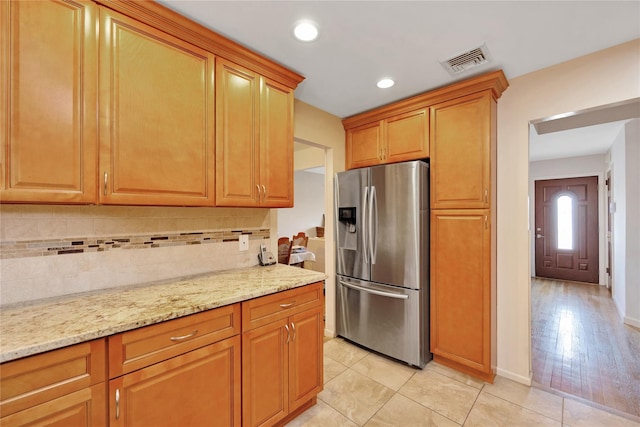 kitchen featuring visible vents, stainless steel refrigerator with ice dispenser, light tile patterned flooring, decorative backsplash, and light stone countertops