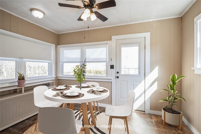 dining area with ornamental molding, radiator heating unit, wood walls, baseboards, and ceiling fan