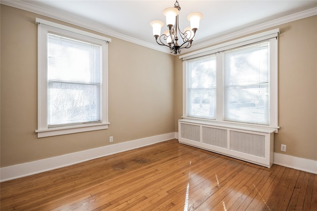 empty room featuring a notable chandelier, plenty of natural light, radiator, and ornamental molding