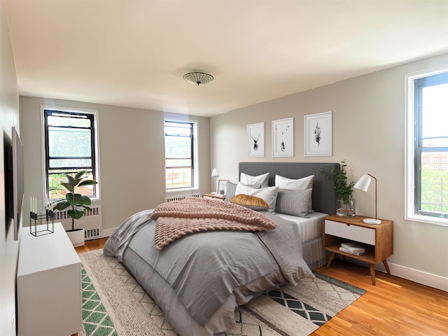 bedroom with multiple windows, radiator heating unit, baseboards, and light wood-type flooring