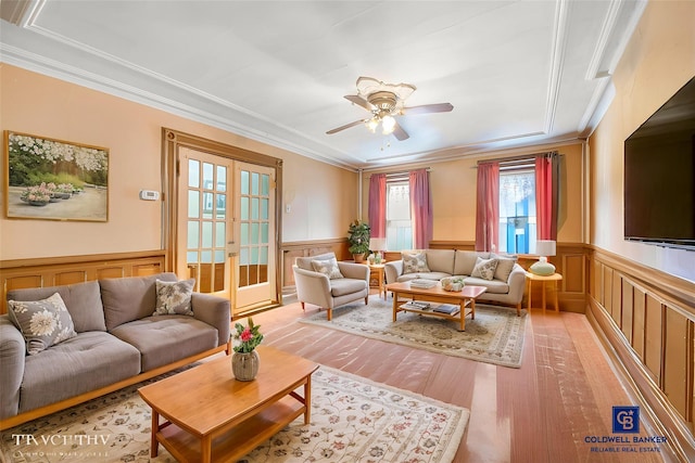 living room with a ceiling fan, a wainscoted wall, ornamental molding, french doors, and light wood-type flooring