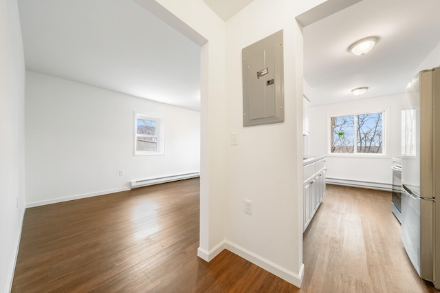 hallway featuring wood finished floors, baseboards, electric panel, a baseboard heating unit, and baseboard heating