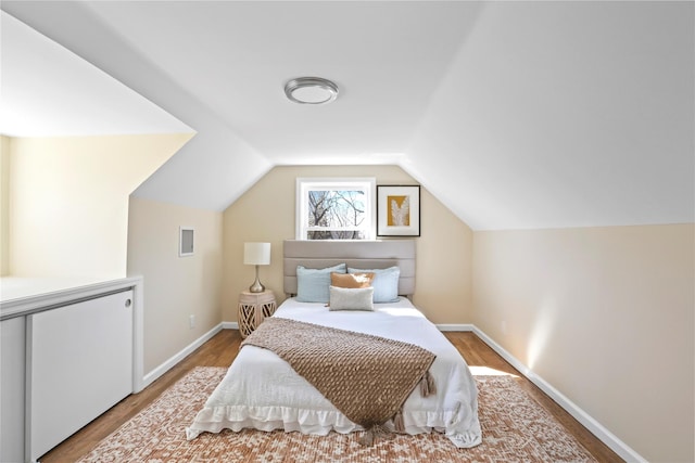 bedroom with vaulted ceiling, baseboards, and wood finished floors