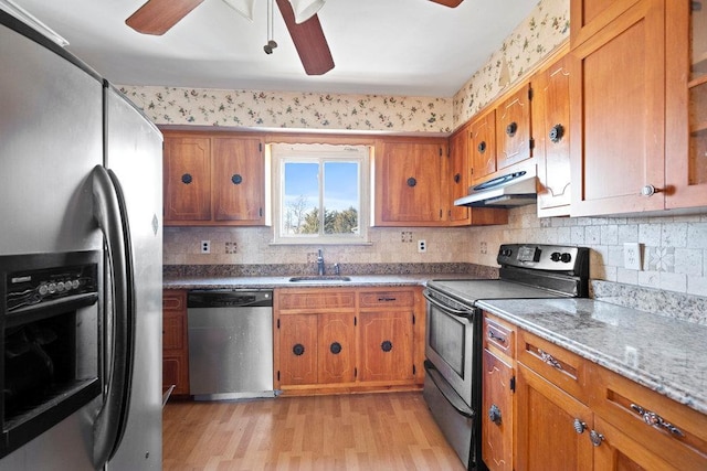 kitchen with under cabinet range hood, appliances with stainless steel finishes, brown cabinetry, and a sink