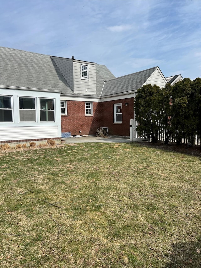 rear view of property featuring a patio, a lawn, and brick siding