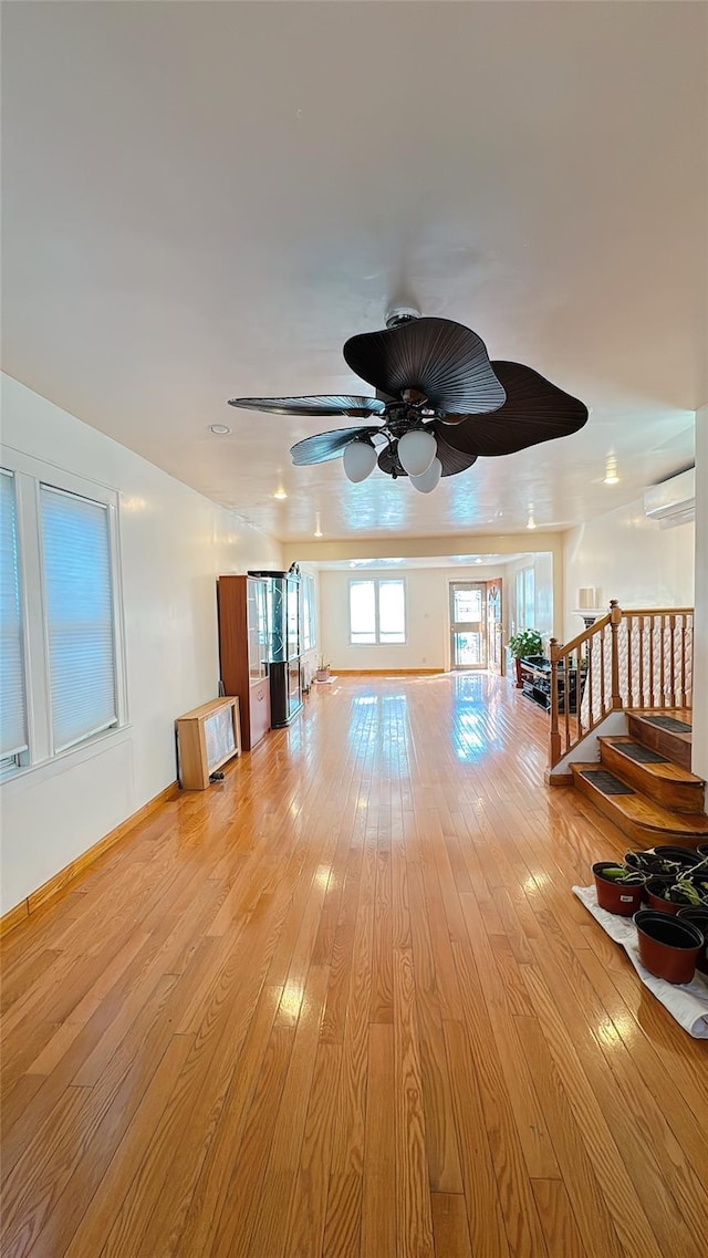 living room featuring a wall mounted air conditioner, stairway, baseboards, and light wood-style floors