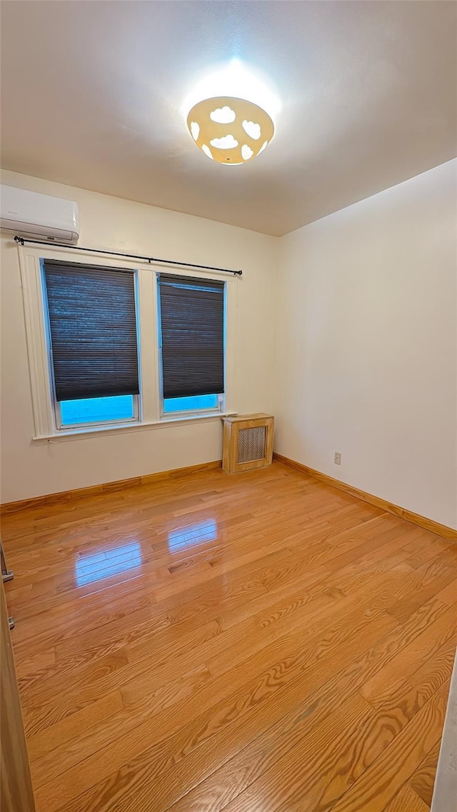 spare room featuring baseboards, light wood-type flooring, and a wall mounted air conditioner