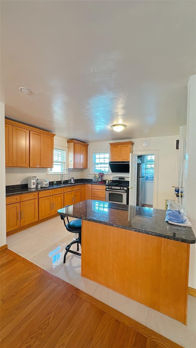 kitchen with stainless steel range with gas cooktop, light wood-type flooring, dark stone countertops, brown cabinetry, and a sink