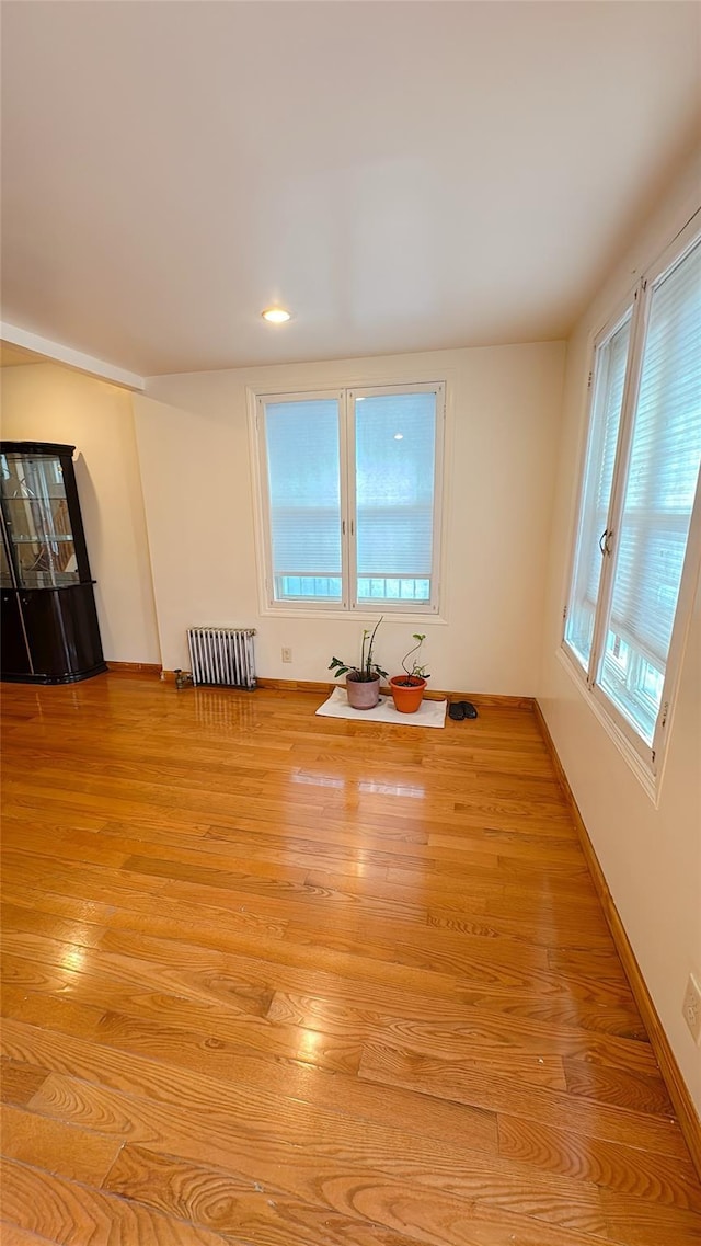 empty room featuring radiator, baseboards, and light wood-type flooring