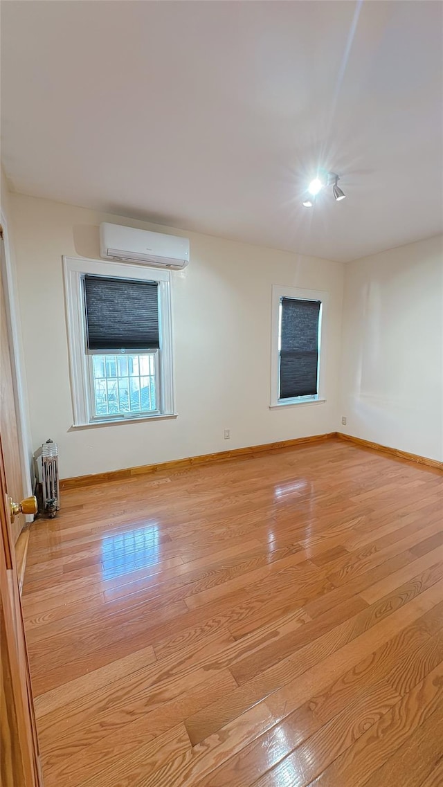 empty room with light wood-type flooring, baseboards, and an AC wall unit