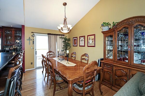 dining area featuring a notable chandelier, light wood-type flooring, indoor bar, and vaulted ceiling