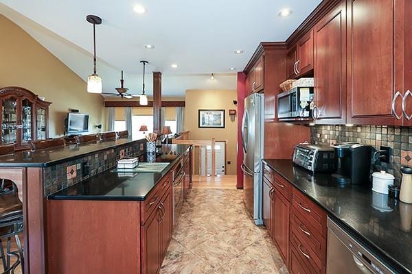 kitchen with dark countertops, tasteful backsplash, a center island, appliances with stainless steel finishes, and a kitchen breakfast bar