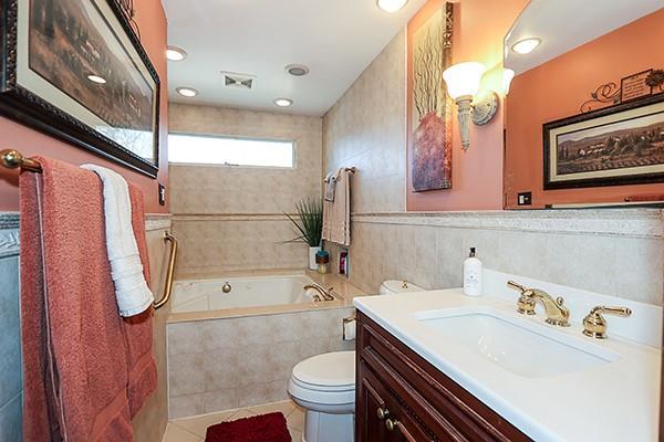 bathroom with tiled bath, tile walls, toilet, tile patterned floors, and vanity