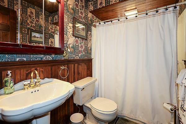 bathroom with curtained shower, wallpapered walls, a wainscoted wall, toilet, and a sink