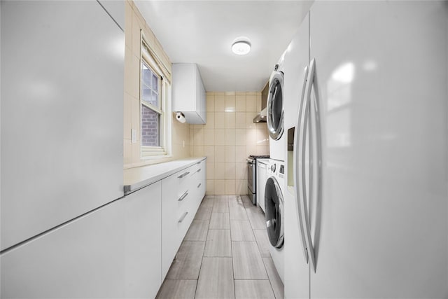 laundry room featuring tile walls, stacked washer and clothes dryer, and laundry area