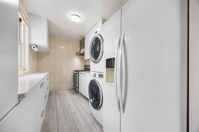 washroom with light tile patterned floors, tile walls, and stacked washer and dryer