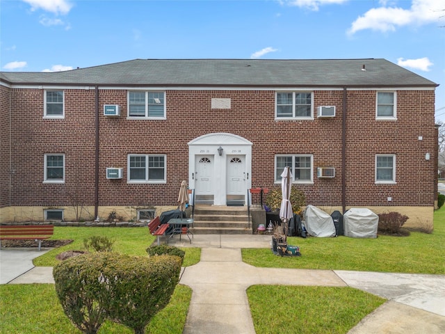 view of front of house featuring a front yard, a wall unit AC, and brick siding