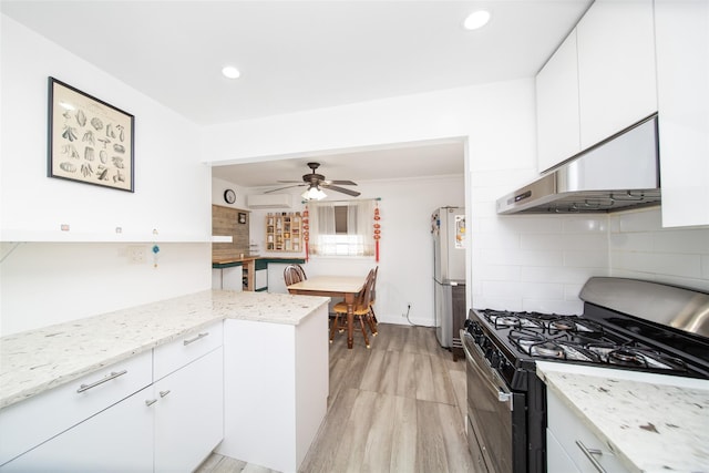 kitchen with tasteful backsplash, under cabinet range hood, gas range, freestanding refrigerator, and white cabinetry