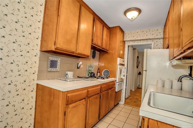 kitchen with wallpapered walls, a sink, light countertops, white oven, and a warming drawer