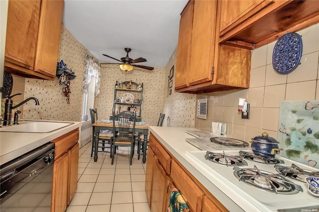 kitchen with a sink, brown cabinetry, wallpapered walls, dishwasher, and white gas stovetop