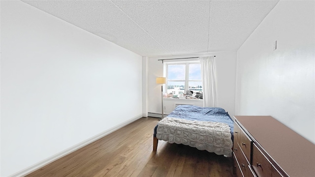 bedroom featuring baseboards, baseboard heating, light wood-style flooring, and a textured ceiling