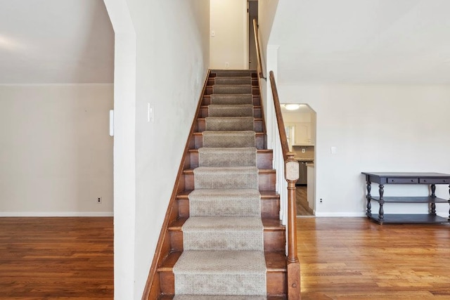 staircase with arched walkways, crown molding, baseboards, and wood finished floors