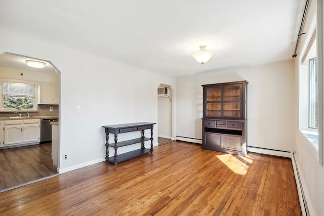 unfurnished living room with arched walkways, baseboard heating, a healthy amount of sunlight, and light wood-style floors