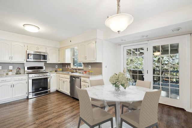 kitchen with light countertops, dark wood-style flooring, appliances with stainless steel finishes, hanging light fixtures, and a sink