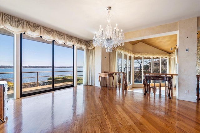 unfurnished dining area with a water view, lofted ceiling, wood finished floors, and a notable chandelier