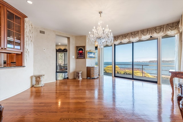 unfurnished dining area featuring a chandelier, wood finished floors, visible vents, a water view, and recessed lighting