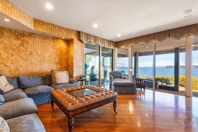 living room featuring wallpapered walls, wood finished floors, a water view, and a healthy amount of sunlight