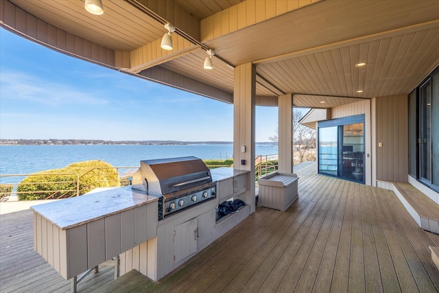 wooden deck with an outdoor kitchen, a water view, and a grill