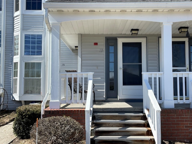 view of exterior entry featuring covered porch and roof with shingles