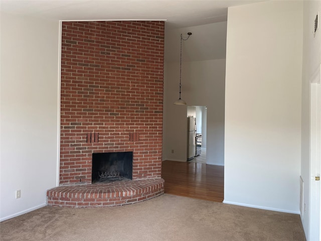 unfurnished living room featuring a high ceiling, a brick fireplace, carpet flooring, and baseboards