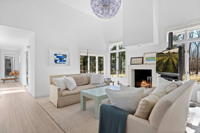 living room featuring hardwood / wood-style floors, baseboards, a high ceiling, a warm lit fireplace, and a notable chandelier