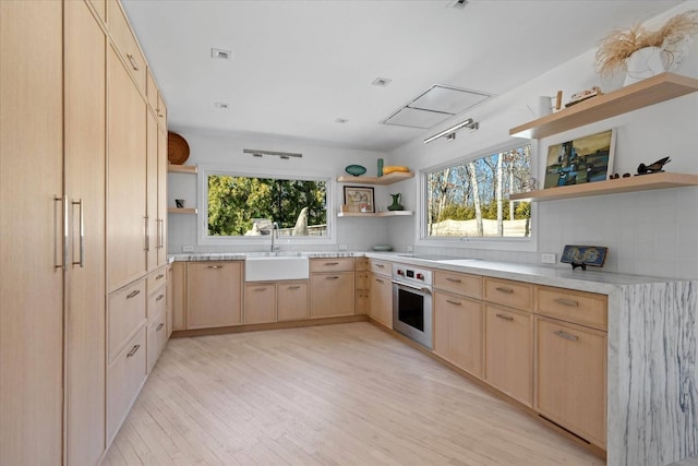 kitchen featuring open shelves, oven, light brown cabinetry, light countertops, and a sink