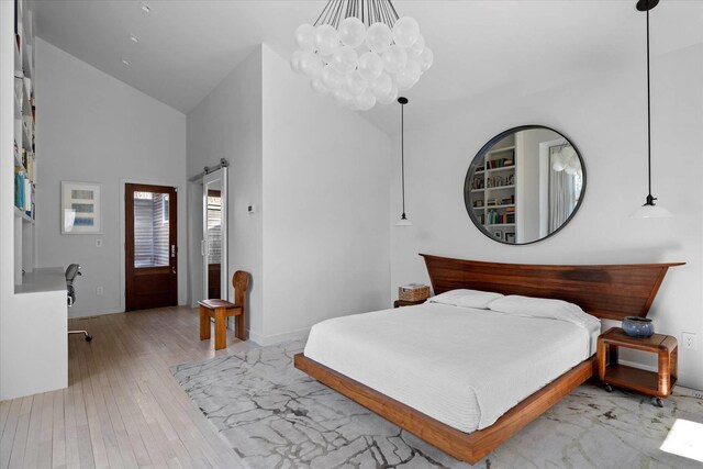 bedroom with a barn door, wood-type flooring, high vaulted ceiling, and an inviting chandelier