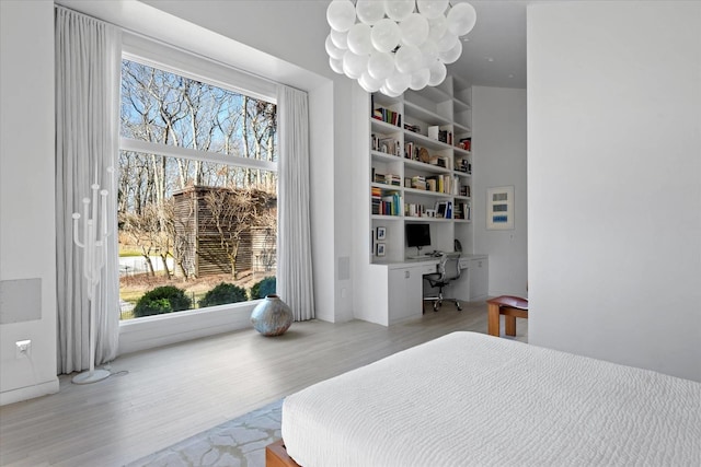 bedroom featuring light wood finished floors, a chandelier, and built in study area