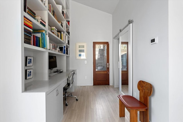 home office featuring a barn door, built in desk, baseboards, and light wood-style floors