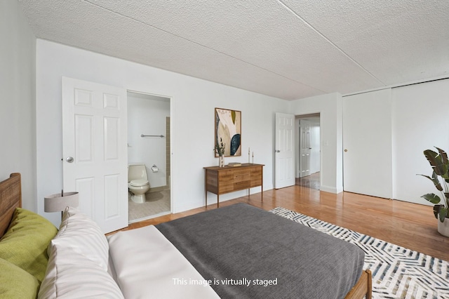 bedroom with a textured ceiling, ensuite bathroom, a closet, and wood finished floors
