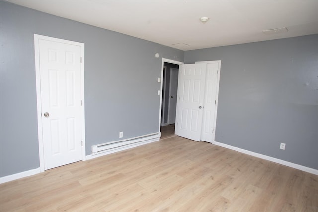 unfurnished bedroom featuring a baseboard heating unit, baseboards, and light wood-type flooring