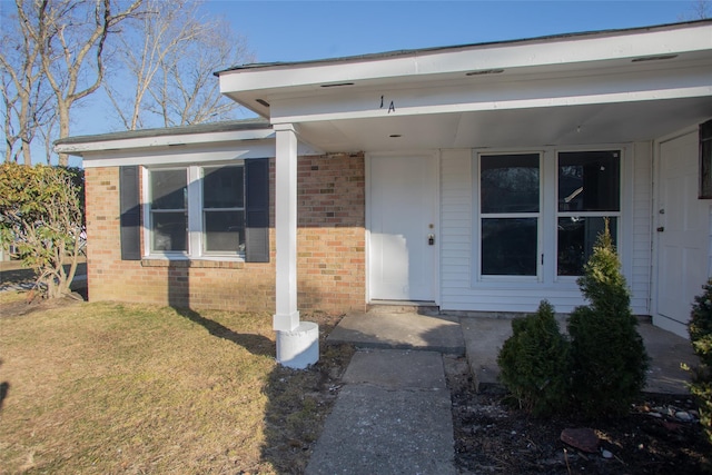 doorway to property featuring a yard and brick siding