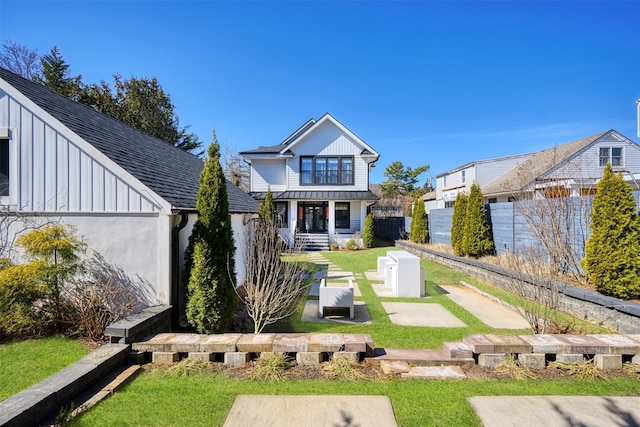 back of property with board and batten siding, a shingled roof, a yard, and fence