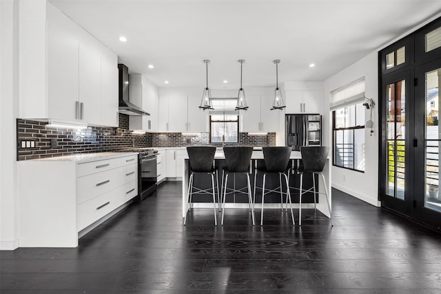 kitchen featuring tasteful backsplash, gas range oven, a breakfast bar area, stainless steel fridge with ice dispenser, and wall chimney range hood