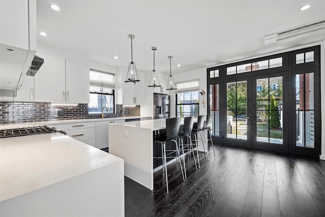 kitchen featuring a kitchen island, dark wood-type flooring, stainless steel fridge with ice dispenser, decorative backsplash, and a sink