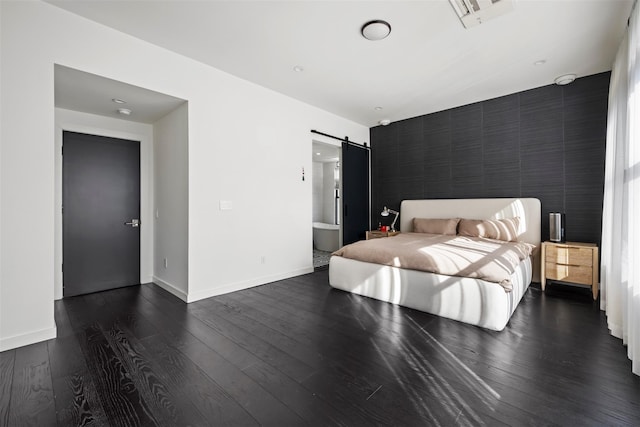 bedroom featuring dark wood-style floors, baseboards, visible vents, an accent wall, and a barn door